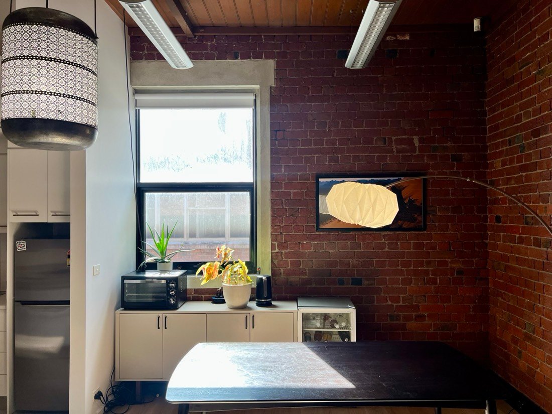 A tall window and exposed brick corner with a floor lamp and framed artwork